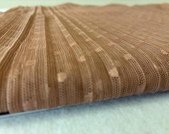 May include: Close-up of a folded, sheer fabric in a warm, light brown hue. The material has a ribbed texture with small, square perforations evenly spaced throughout. The fabric appears soft and delicate, with a slight sheen.