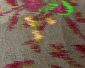 May include: A gray fabric with a floral pattern in shades of magenta, green, and peach. The design appears to be hand-painted or printed, with a slightly blurred effect. The fabric has a subtle sheen.