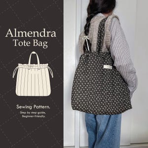 Puede incluir: Un bolso tote negro con un estampado floral blanco se lleva sobre el hombro. El bolso tiene un cierre de cordón y una etiqueta blanca. La imagen también muestra un dibujo del bolso y el texto "Almendra Tote Bag" y "Sewing Pattern."