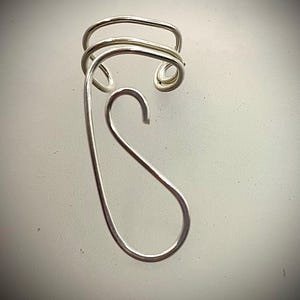 May include: A silver wire ring with a unique, abstract design. The ring is made of a single piece of wire that is twisted and bent into a complex shape.