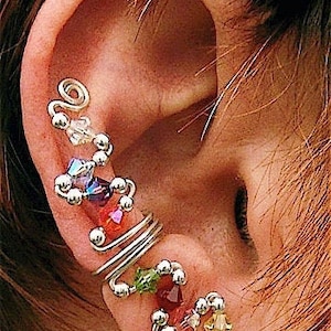 May include: Silver ear cuff with colorful beads and crystals. The cuff is designed to wrap around the ear and features a variety of beads and crystals in different colors, including red, green, blue, and clear.