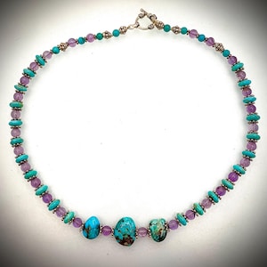 Könnte beinhalten: Eine türkisfarbene und amethystfarbene Perlenkette mit einem silbernen Verschluss. Die Kette hat drei große Türkis-Steine.