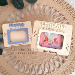 May include: Two wooden photo frames, one reading "Mama WE LOVE YOU" with a blue scalloped frame, and the other reading "Grandma I LOVE YOU" with a white scalloped frame. Both frames have heart details and are personalized.