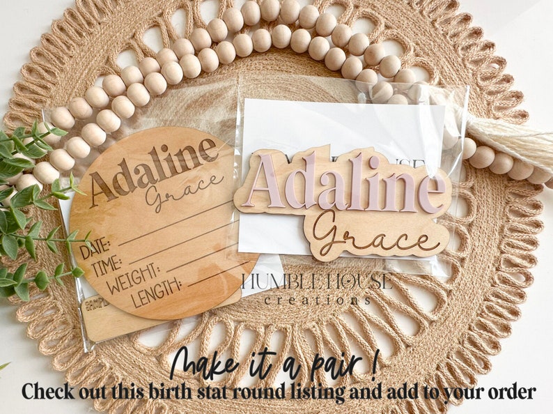 May include: A set of two wooden name plaques with the name "Adaline Grace" in pink and brown lettering. The larger plaque is a round birth stat plaque with lines for date, time, weight, and length. The smaller plaque is a rectangular name plaque. The plaques are packaged together in a clear plastic bag.