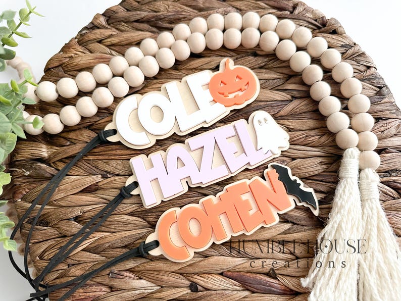 May include: Three wooden Halloween name tags with black string. The names are Cole, Hazel, and Cohen. Each tag has a Halloween-themed cutout: a pumpkin, a ghost, and a bat.