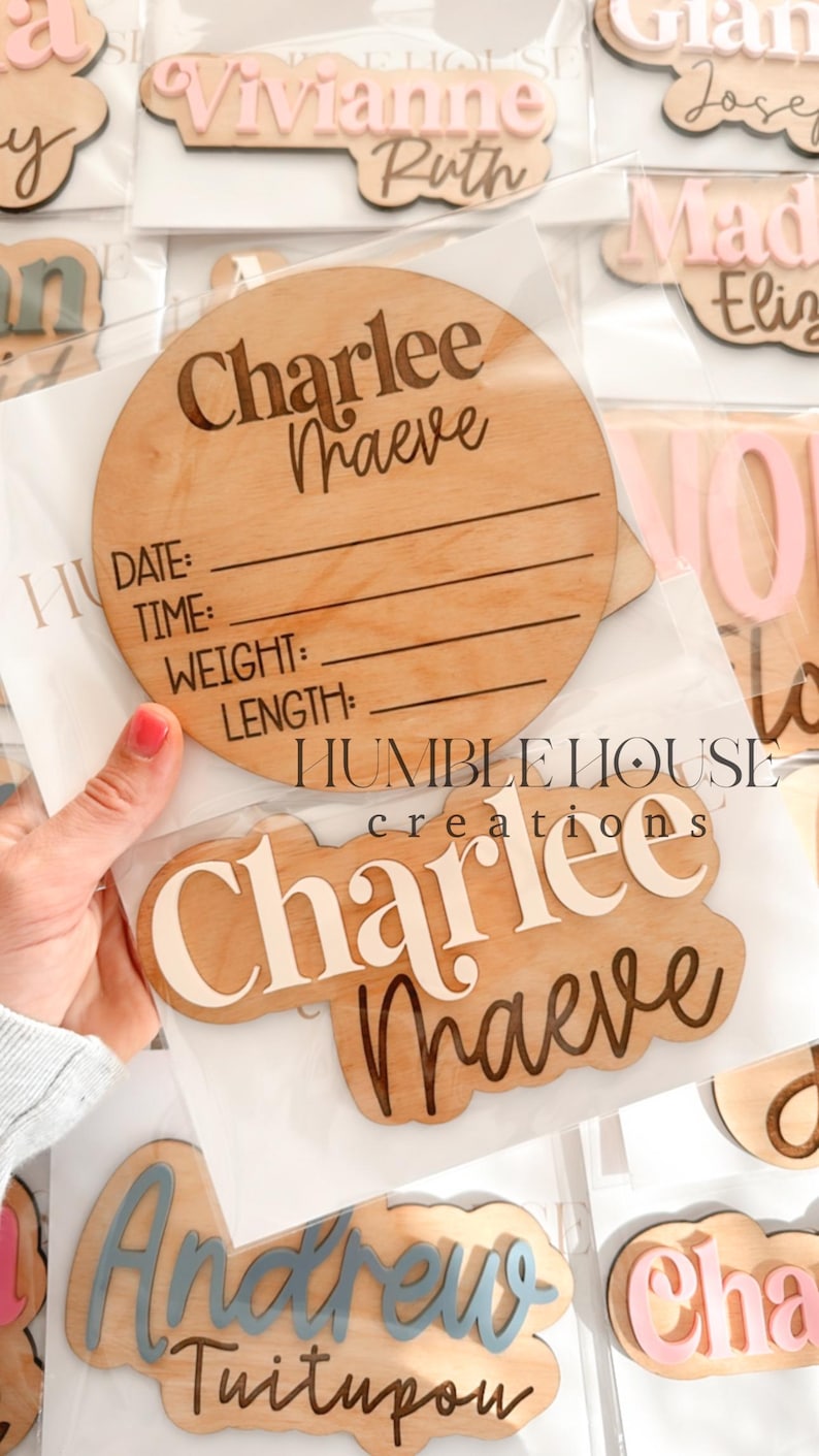 May include: A set of wooden baby name plaques with various names and fonts. The plaques are in different shapes and sizes, and some have a space for birth information. The plaques are in a variety of colors, including pink, blue, and white.