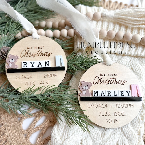 Puede incluir: Dos adornos navideños de madera con un diseño de osito de peluche. Los adornos están personalizados con los nombres "Ryan" y "Marley" e incluyen detalles de nacimiento como la fecha, el peso y la longitud. Los adornos están decorados con acentos rosas y blancos.