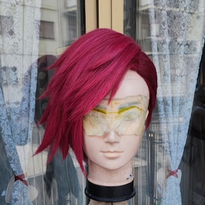 May include: A pink wig on a mannequin head with tape over the eyes. The mannequin is on a tripod stand.