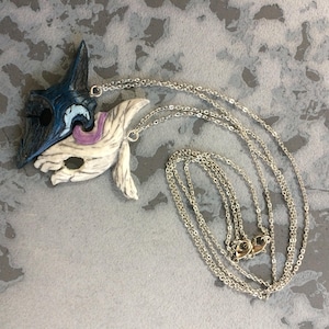 May include: A silver chain necklace with two pendants, one blue and one white, shaped like masks. The masks are connected together.