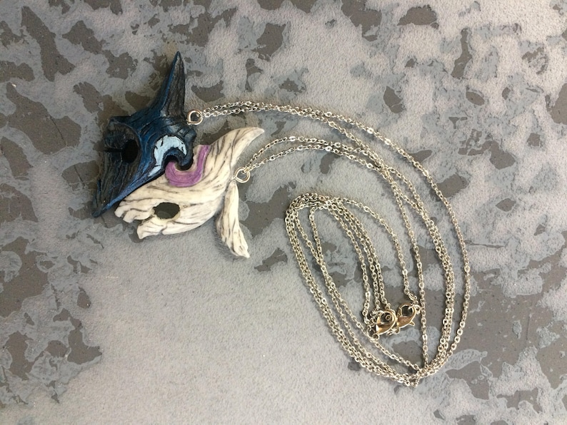 May include: A silver chain necklace with two pendants, one blue and one white, shaped like masks. The masks are connected together.