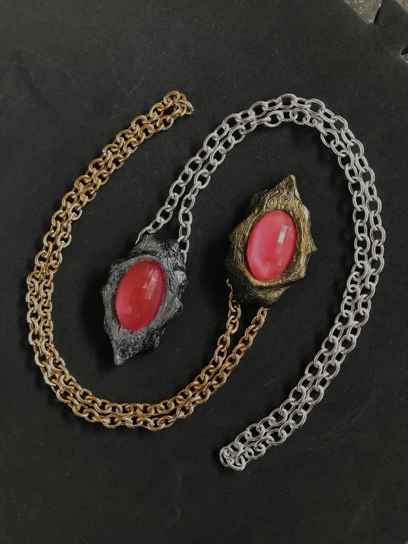 Pode incluir: Dois colares com pingentes de gemas cor-de-rosa. Um colar tem uma corrente de ouro e um pingente de ouro com uma gema cor-de-rosa. O outro colar tem uma corrente de prata e um pingente de prata com uma gema cor-de-rosa.