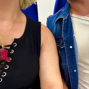 May include: Two gold chain necklaces with pendant charms. One pendant is a red, leaf-shaped charm, and the other is a blue, teardrop-shaped charm. The necklaces are worn over black and white tops.