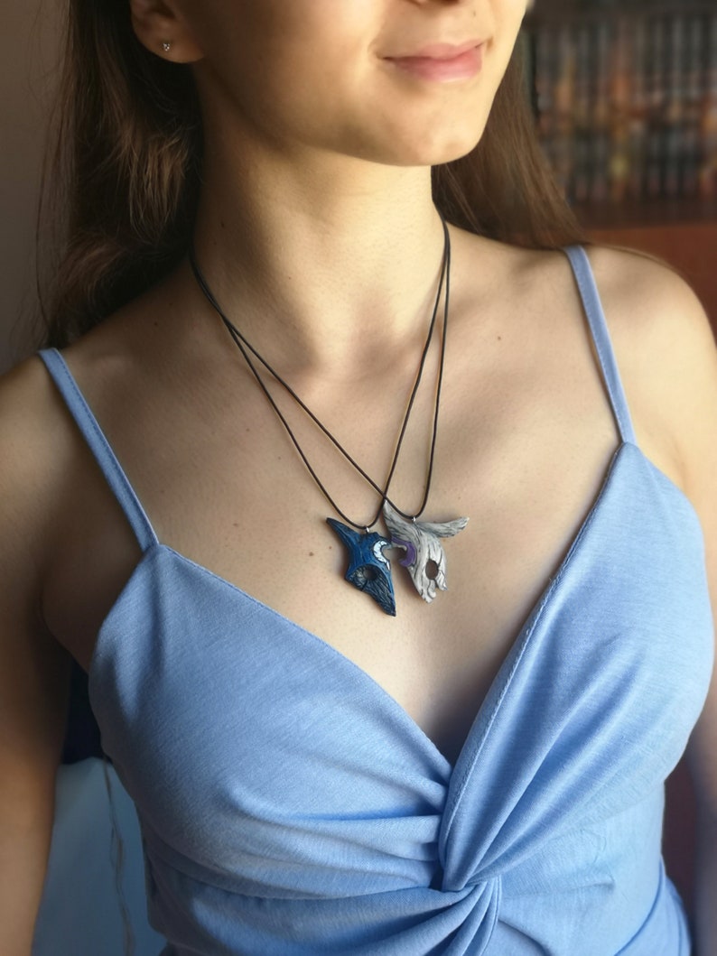 May include: Two necklaces with silver and blue wolf mask pendants. The masks are detailed and have a textured finish. The necklaces are worn by a person with a blue top.