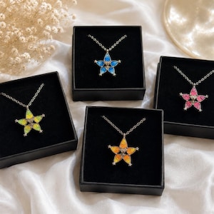 May include: Four star-shaped pendants on silver-toned chains, each presented in a black square box. The pendants feature colourful, textured centres in blue, pink, yellow, and green, with small silver star accents at each point of the star shape.