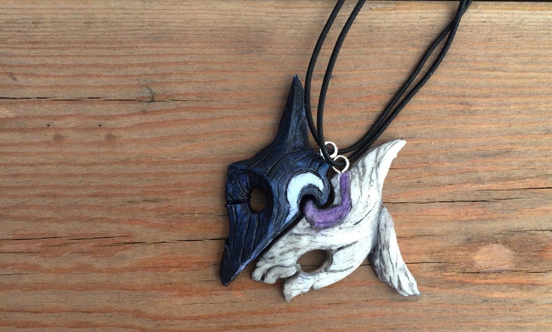 May include: A pair of black and white wolf masks on a black cord necklace. The masks are connected and have a purple and white design.