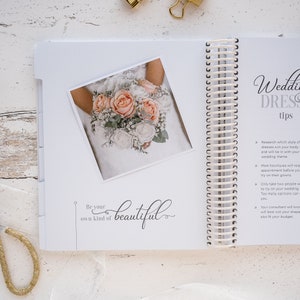 May include: A white wedding dress with a bouquet of pink and white flowers. The text "Be your own kind of beautiful" is written below the image. The page is from a wedding planning book with tips for choosing a wedding dress.