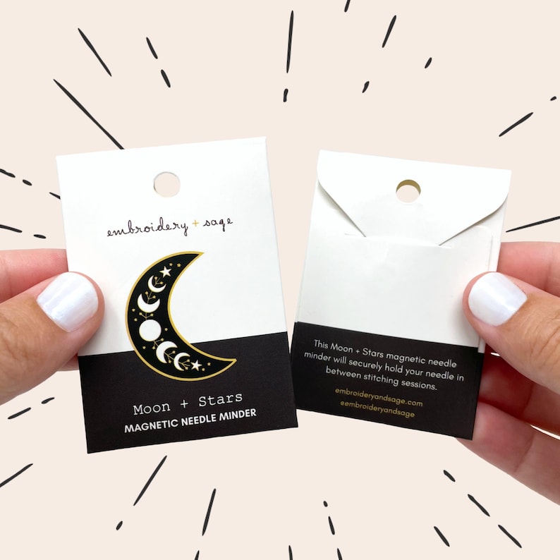 May include: A black and gold magnetic needle minder with a crescent moon and star design. The card reads "Moon + Stars MAGNETIC NEEDLE MINDER" and "embroidery + sage". The minder securely holds needles between stitching sessions.