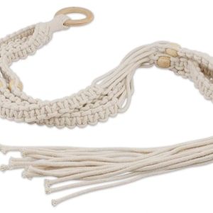 Pode incluir: Um suporte de plantas de macramé branco com contas de madeira e um anel de metal dourado. O suporte tem uma franja longa.