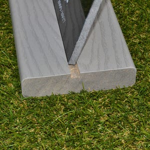 May include: Close-up of a gray wooden sign holder with a black sign inserted. The sign holder has a groove in the center and is sitting on a green artificial grass surface.