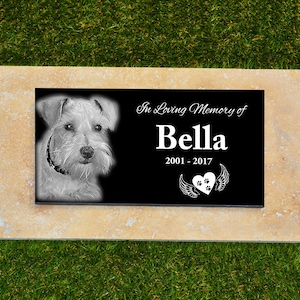 May include: Black granite pet memorial with a photo of a white dog, the text "In Loving Memory of Bella 2001-2017" and a heart with paw prints and wings.