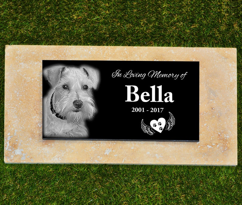 May include: Black granite pet memorial with a photo of a white dog, the text "In Loving Memory of Bella 2001-2017" and a heart with paw prints and wings.