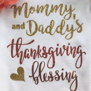 Peut inclure: Une grenouill&egrave;re blanche avec l'inscription "Mommy and Daddy's Thanksgiving Blessing" en lettres paillet&eacute;es dor&eacute;es et un c&oelig;ur paillet&eacute; dor&eacute;.