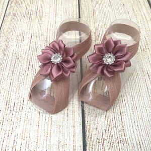 May include: A pair of mauve-colored elastic baby sandals with a satin flower embellishment and a rhinestone center.