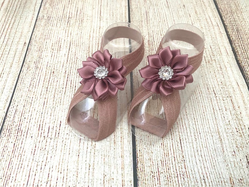 May include: A pair of mauve-colored elastic baby sandals with a satin flower embellishment and a rhinestone center.