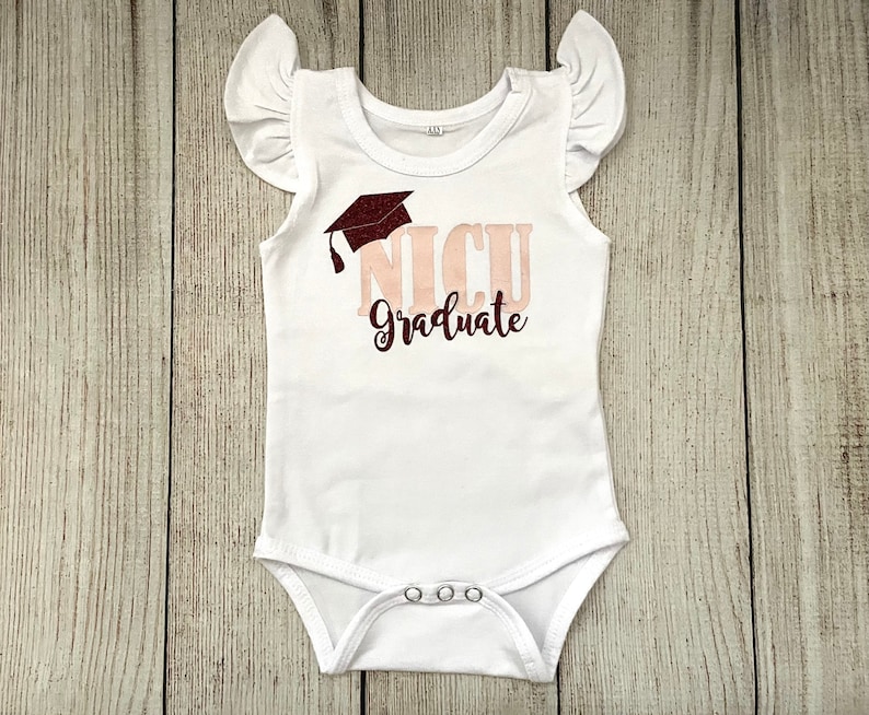 May include: White baby onesie with a pink and maroon graphic that says "NICU Graduate" with a graduation cap above the text.