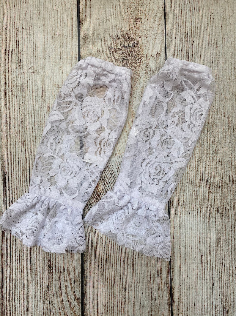 May include: Two white lace arm warmers with a floral pattern and ruffled edges.