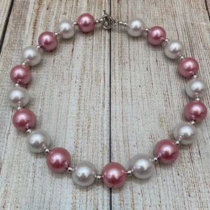 May include: A pink and white pearl necklace with a silver clasp. The pearls are large and round.