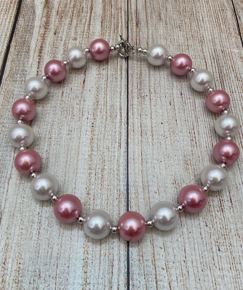 May include: A pink and white pearl necklace with a silver clasp. The pearls are large and round.