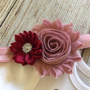 May include: A pink and burgundy flower headband with a rhinestone in the center of the burgundy flower.