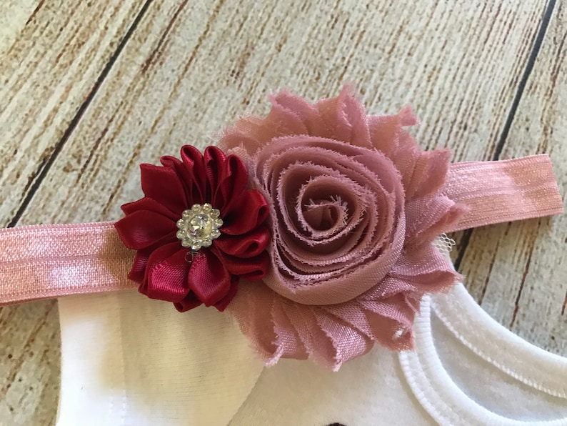 May include: A pink and burgundy flower headband with a rhinestone in the center of the burgundy flower.