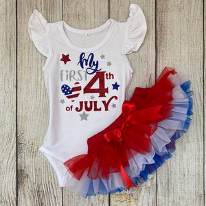 May include: White bodysuit with red, white, and blue glitter accents. The bodysuit says "My First 4th of July". A red, white, and blue tulle skirt with a red bow.