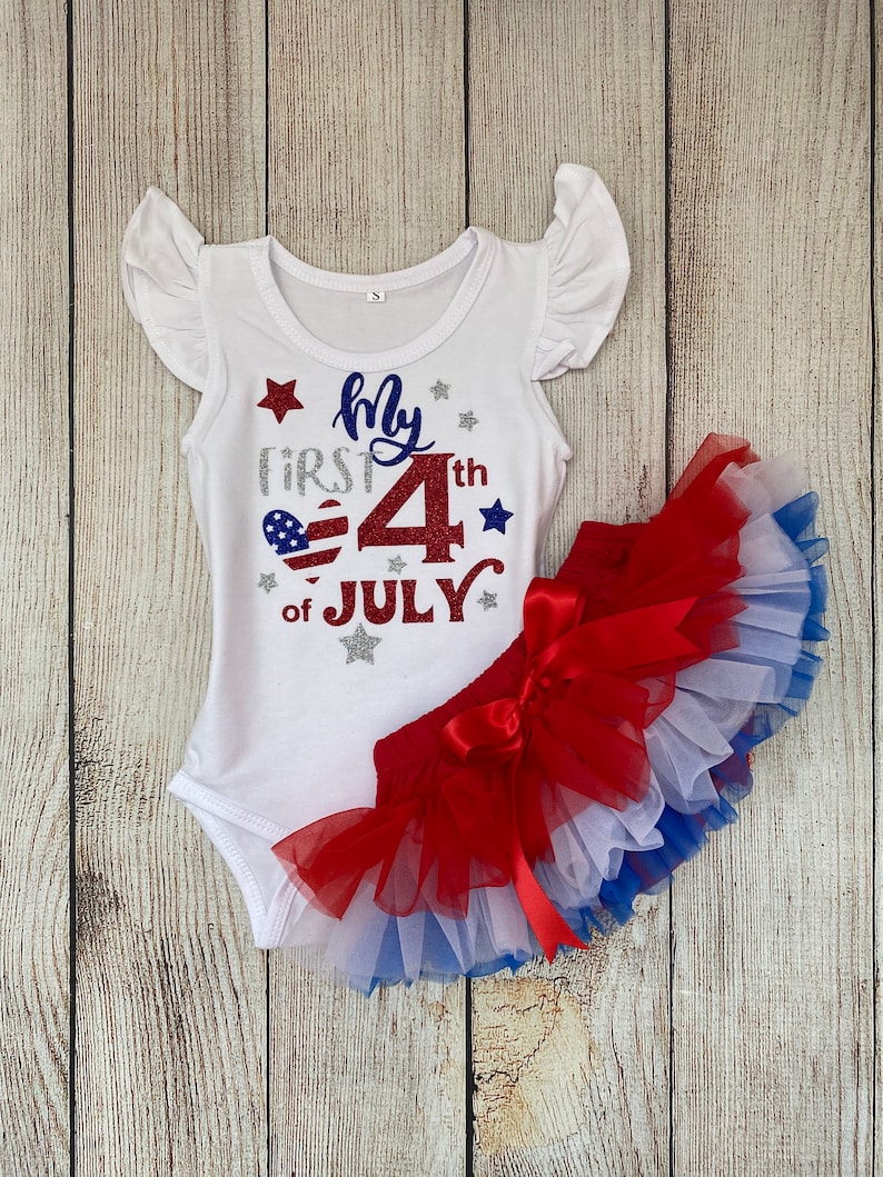 May include: White bodysuit with red, white, and blue glitter accents. The bodysuit says "My First 4th of July". A red, white, and blue tulle skirt with a red bow.