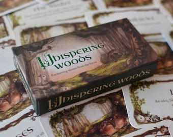 May include: A box of "The Whispering Woods" oracle cards with a green and gold design. The box features a forest scene with trees, a squirrel, and a deer. The text "Enchanting secrets from the forest" is printed on the box.
