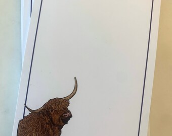 Puede incluir: Una pila de blocs de notas en blanco con una ilustración de una vaca de las tierras altas marrón y blanca en la esquina inferior. Los blocs de notas tienen un borde morado.