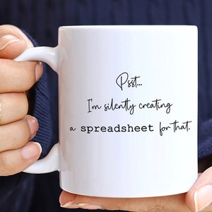 May include: White ceramic mug with a black inscription that reads "Psst... I'm silently creating a spreadsheet for that."