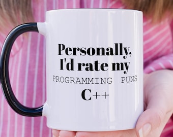 Peut inclure: Un mug en céramique blanche avec une anse noire portant le texte imprimé en noir : Personally, I'd rate my PROGRAMMING PUNS C++. Le mug présente un corps cylindrique et une anse incurvée, offrant une vue claire de la blague informatique.