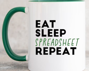 Puede incluir: Una taza de cerámica blanca con asa e interior de color verde oscuro. El frente presenta el texto negro EAT, SLEEP y REPEAT, con la palabra SPREADSHEET impresa en verde entre ellos. El diseño está centrado en la superficie cilíndrica.