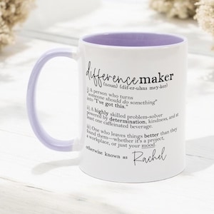 May include: White ceramic mug with a light purple interior and handle. The mug features the definition of "difference maker" in black script, including the name "Rachel" at the bottom. A perfect gift for a friend or family member.