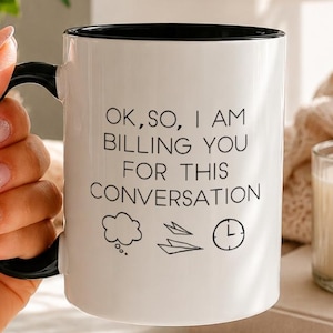May include: A white ceramic mug with a black interior and handle, featuring the black printed text "OK, SO, I AM BILLING YOU FOR THIS CONVERSATION" followed by small line-art icons of a thought bubble, a paper airplane, and a clock face.