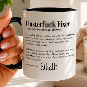 Può includere: Una tazza in ceramica bianca con manico e interno neri, caratterizzata da un testo stampato in nero che definisce il termine Clusterf*ck Fixer. Il testo include una pronuncia fonetica, una definizione umoristica e il nome Eilidh in basso.