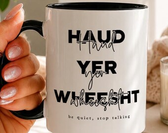May include: A white ceramic mug with a black handle and interior rim. The mug features black text that reads "HAUD YER WHEESHT" in a bold, stylized font, with the smaller script text "be quiet, stop talking" printed underneath.