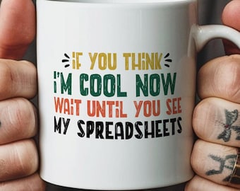 Puede incluir: Una taza de cerámica blanca con el texto "IF YOU THINK I'M COOL NOW WAIT UNTIL YOU SEE MY SPREADSHEETS" impreso en una fuente de estilo retro multicolor. La taza tiene un acabado liso y brillante y un asa curva en el lado derecho.