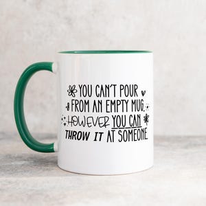 May include: White ceramic mug with a green handle and rim. The mug features black text that reads "YOU CAN'T POUR FROM AN EMPTY MUG. HOWEVER YOU CAN THROW IT AT SOMEONE."
