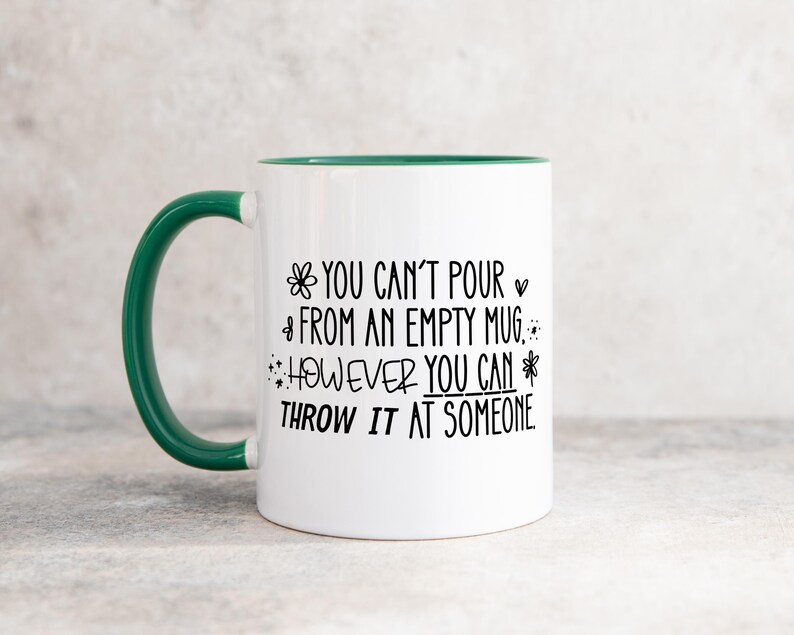 May include: White ceramic mug with a green handle and rim. The mug features black text that reads "YOU CAN'T POUR FROM AN EMPTY MUG. HOWEVER YOU CAN THROW IT AT SOMEONE."
