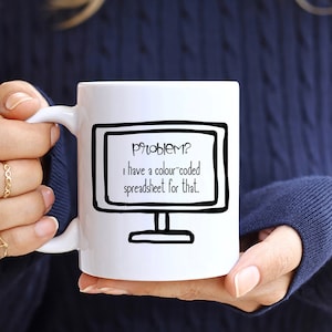 Könnte beinhalten: Eine weiße Keramiktasse mit einer schwarz-weißen Illustration eines Computerbildschirms. Der Text auf dem Bildschirm lautet "Problem? Ich habe eine farbcodierte Tabelle dafür."