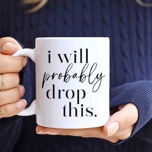 Peut inclure: Une tasse en céramique blanche avec du texte noir qui dit "i will probably drop this."